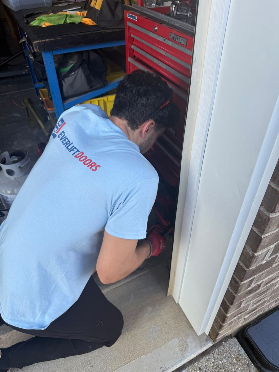 EverLift Doors technician kneeling to repair a garage door frame and track at a Kentucky brick home