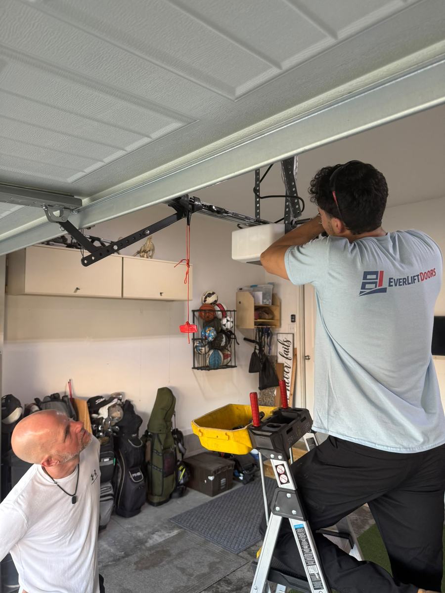 EverLift Doors technician on a ladder repairing a garage door opener while the homeowner watches in a Kentucky garage