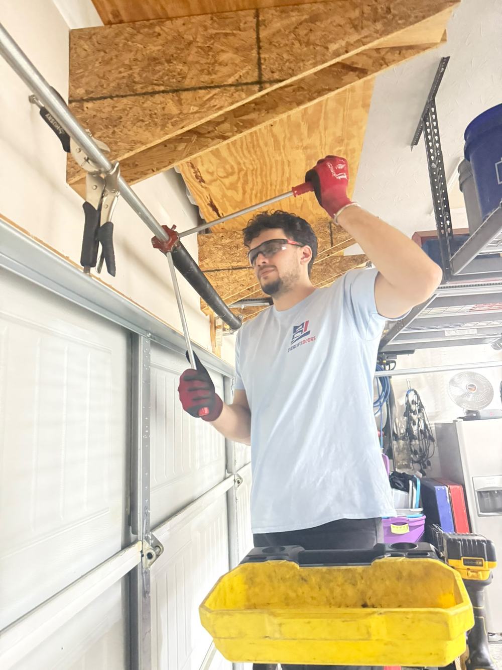 EverLift Doors technician in safety glasses winding a new torsion spring with winding bars during a residential garage door spring replacement in Kentucky